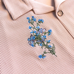 Ryoko Rain Ivory pleated button-up. Close-up of blue floral embroidery on right chest