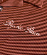 Close-up photo of Ryoko Rain cursive logo on cocoa pleated button-up shirt. 