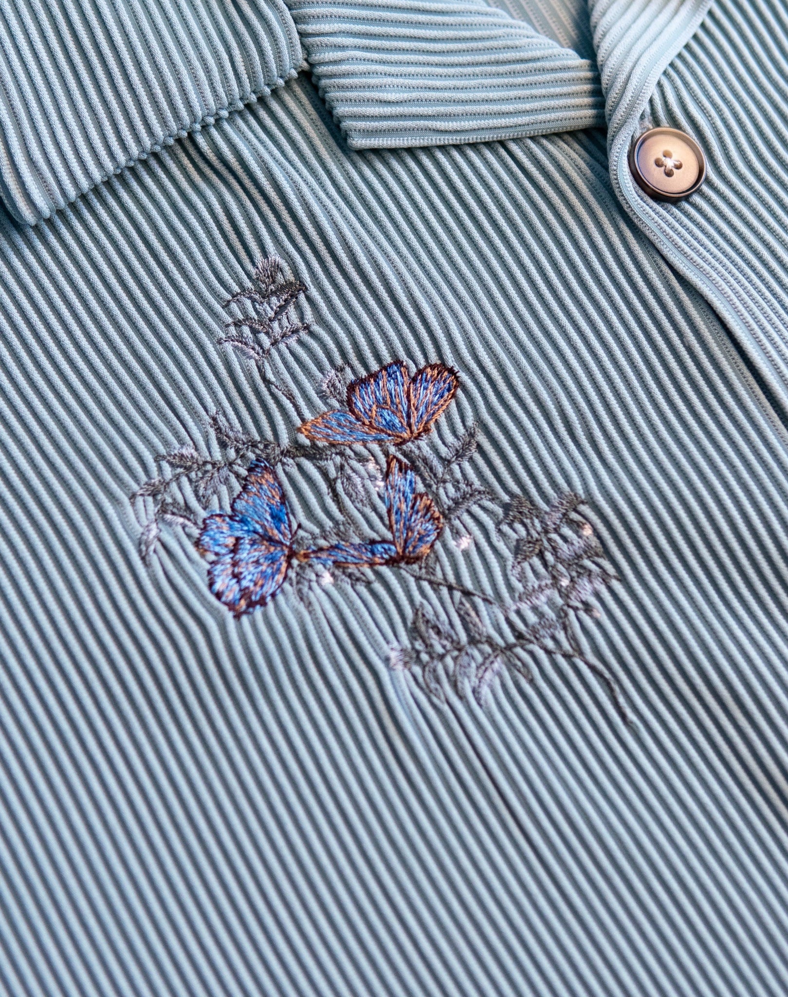 Ryoko Rain Ice Pleated button-up shirt. Close-up of blue floral embroidery on right chest.